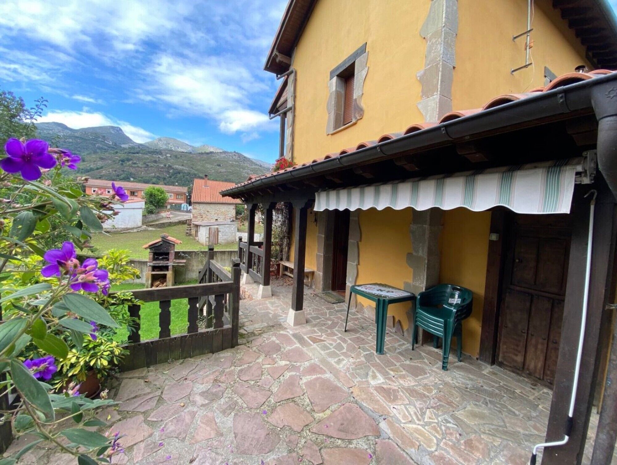 Un edificio amarillo con un patio empedrado de piedra, una valla de madera y vistas a montañas.
