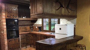 A kitchen with wooden cabinets, a brick oven, a coffee maker, and a refrigerator.