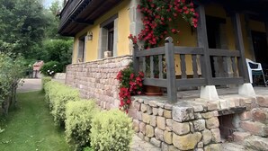 A two-story building with a balcony, stone foundation, and a flower box with red flowers.