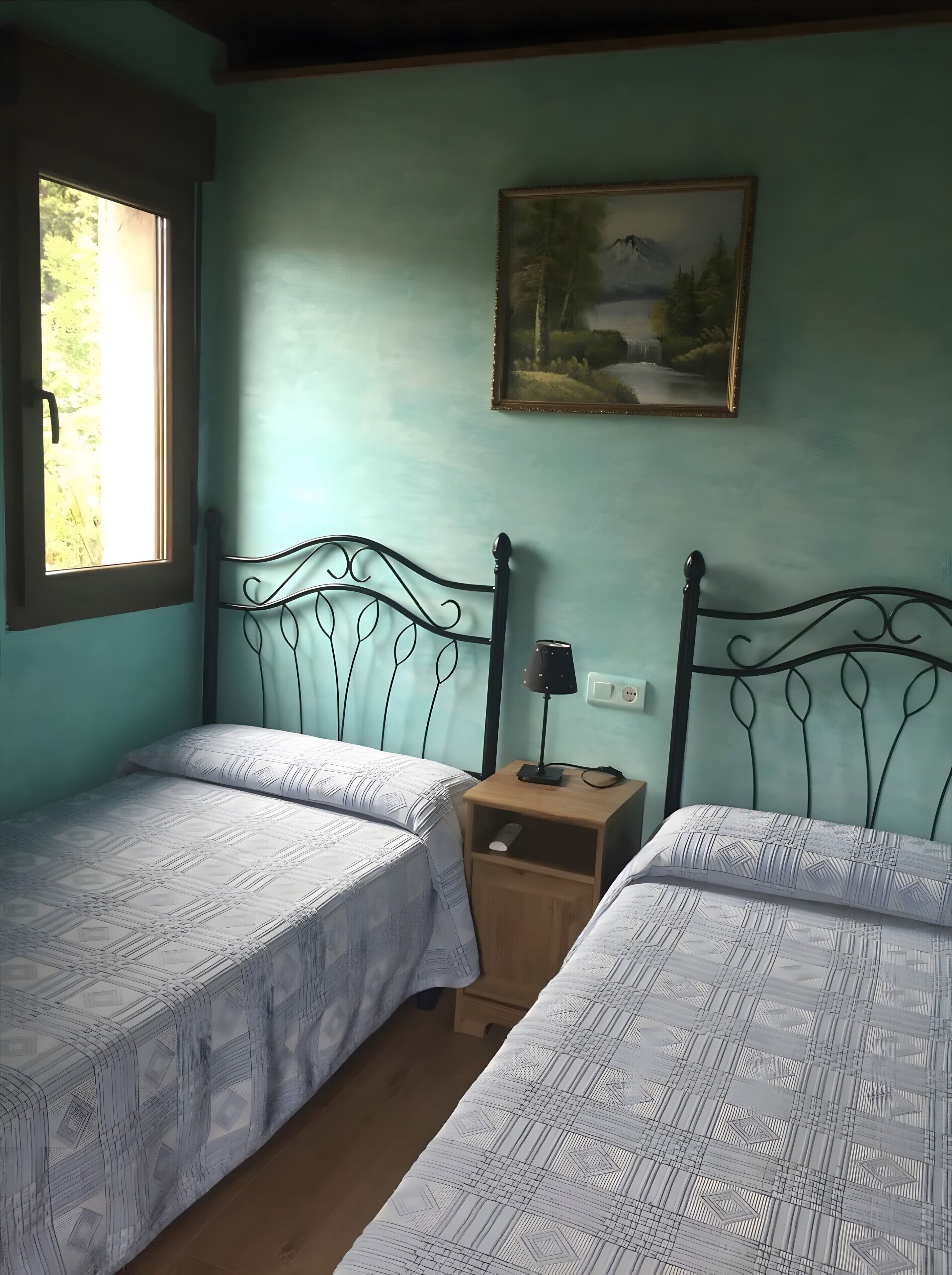 A room with two beds, a nightstand, a lamp, a painting, and a window.