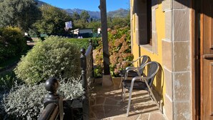 A building with a yellow exterior, a balcony with chairs, and a view of mountains.