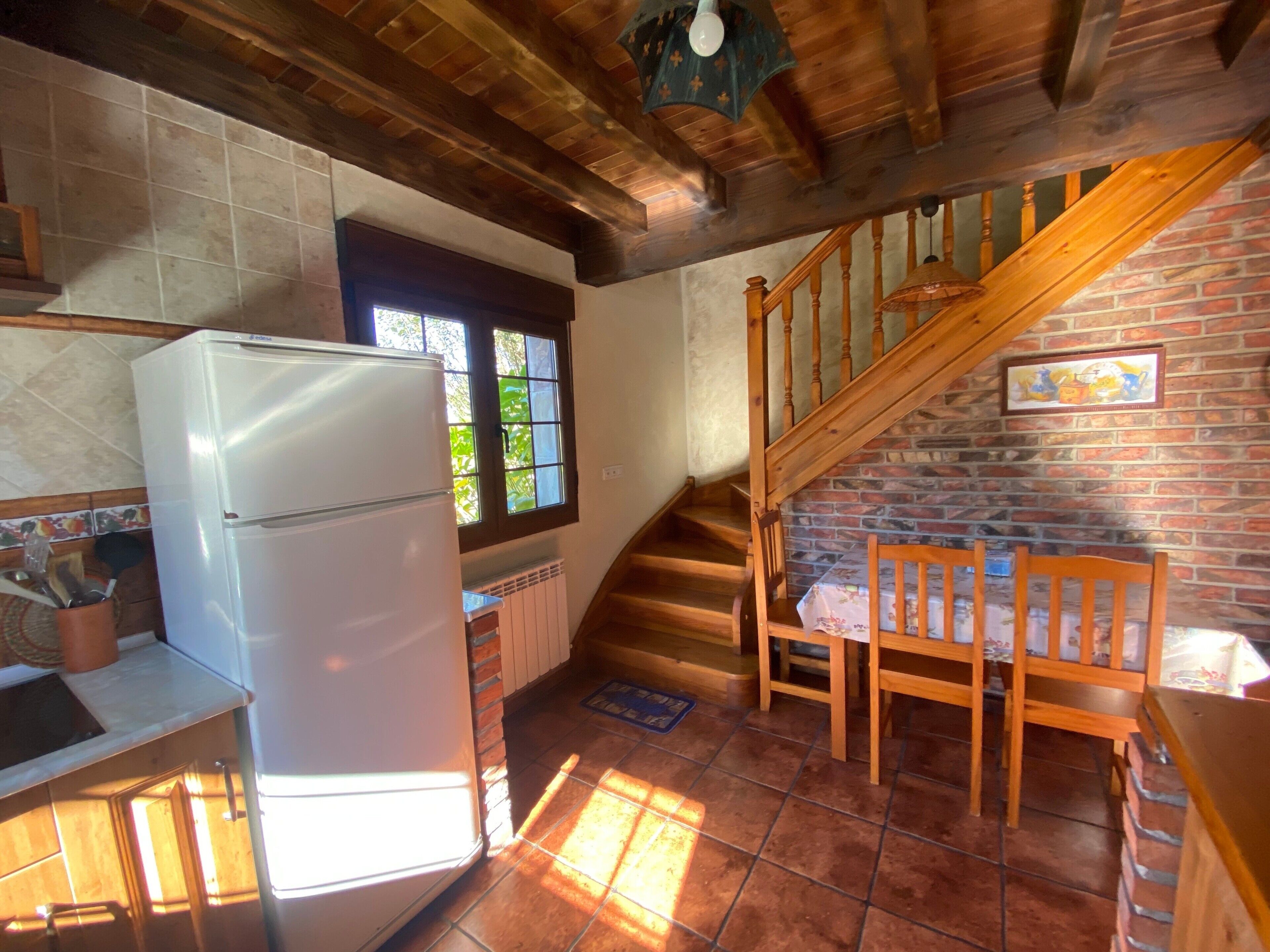 Una cocina con refrigerador, ventana, escalera y comedor.
