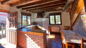 A rustic kitchen with a brick island, wooden beams, a refrigerator, and a dining area with a table and chairs.