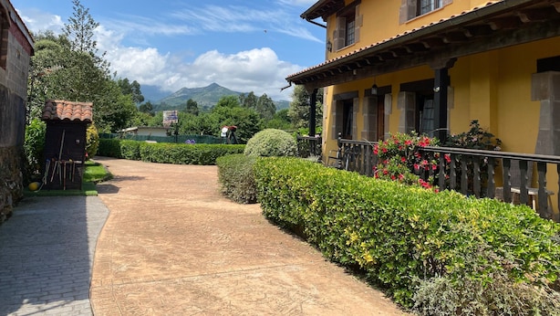 A courtyard with a paved walkway, a yellow building with a balcony, and a mountain in the background.