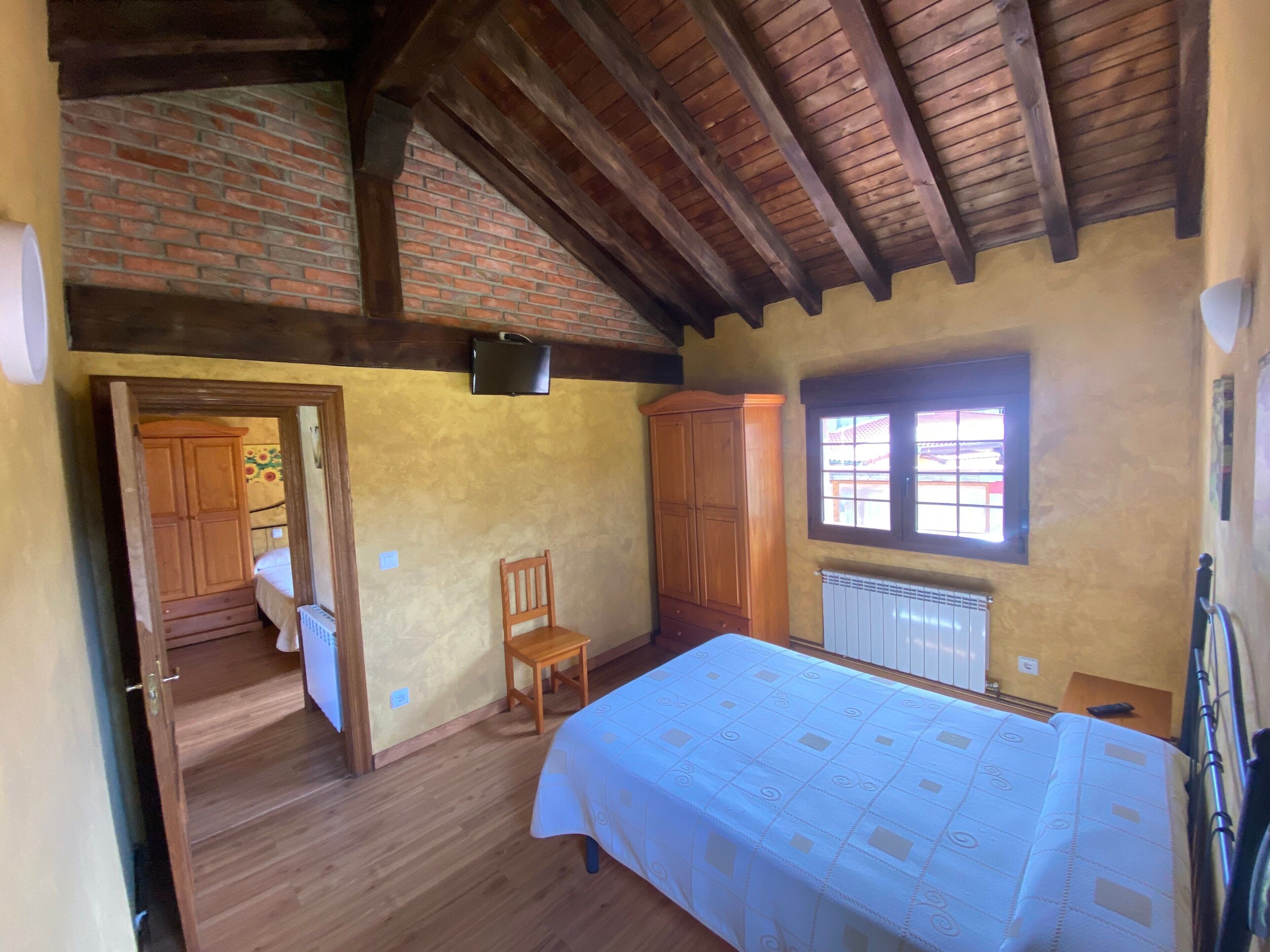 Ein Schlafzimmer mit Holzboden, Backsteinwand, Fenster, Bett, Stuhl und Kleiderschrank.