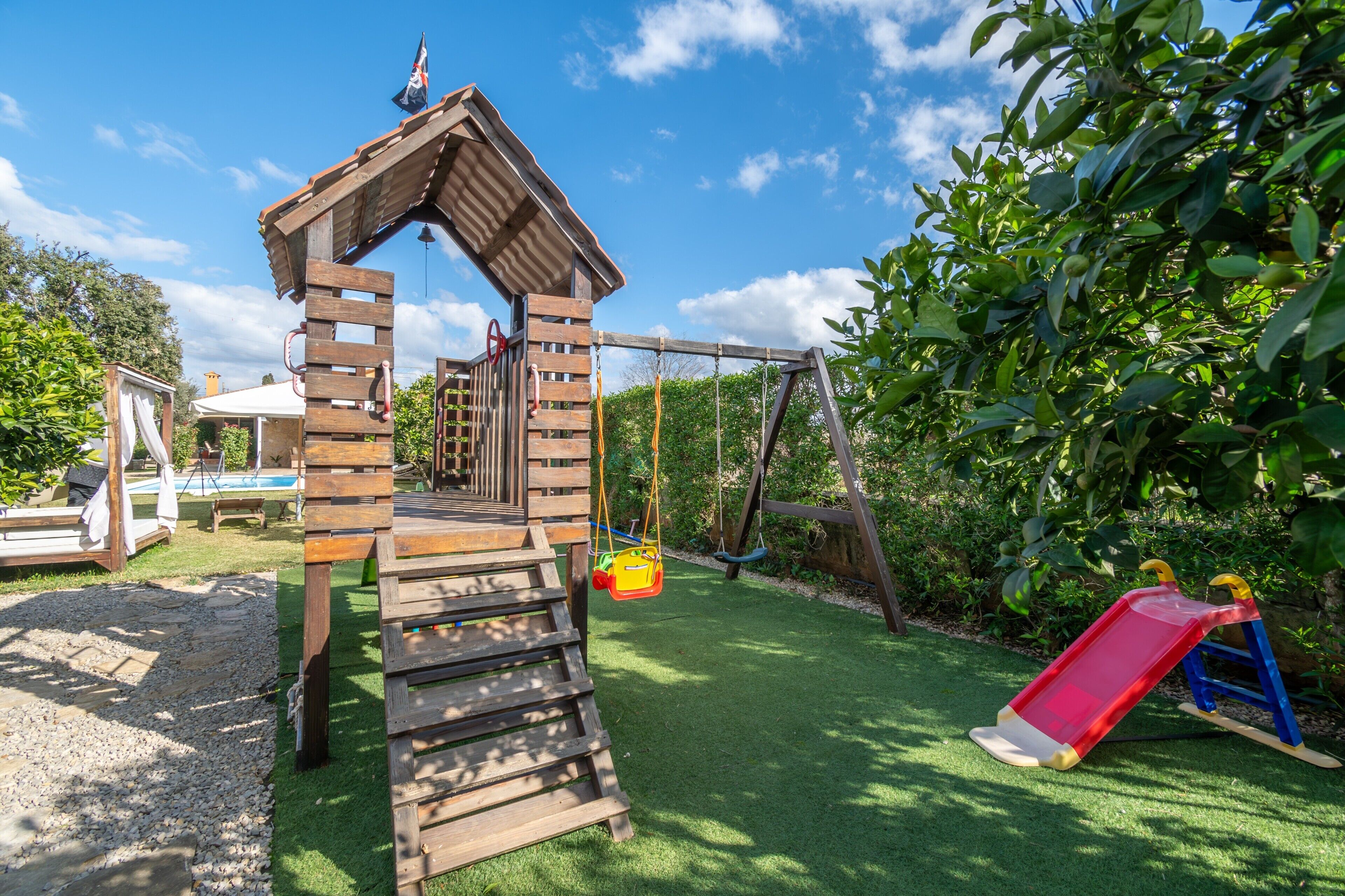 A wooden play structure with a slide, swings, and a small bridge.