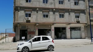 A multi-story building with a gated entrance, a parked white car, and construction materials visible inside.