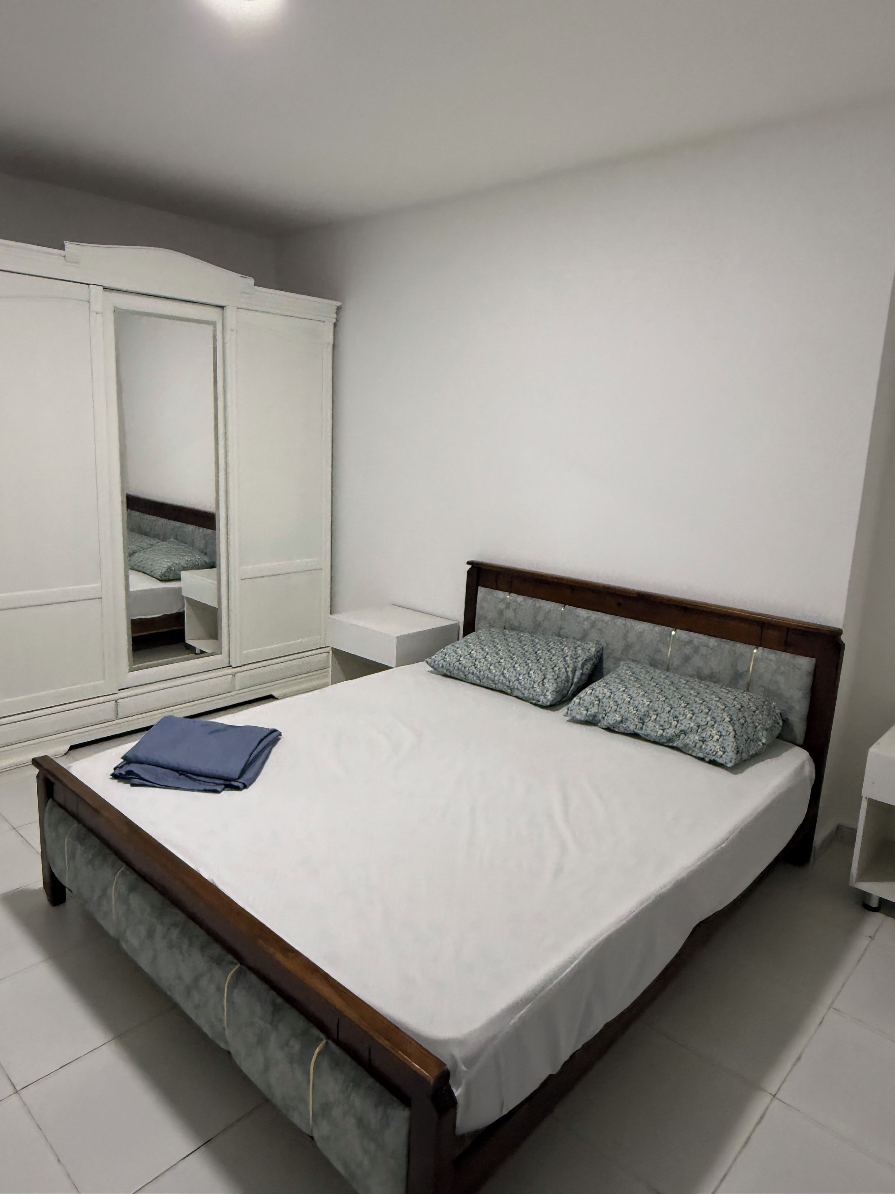 Un dormitorio con una cama, un armario y una mesita de noche.