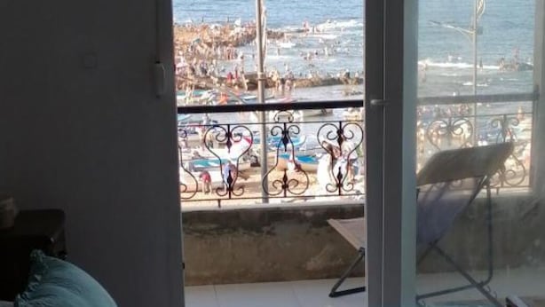 A room with a bed, a window with a view of a crowded beach and the sea. - HOTEL NASSMA residence  (Jijel)