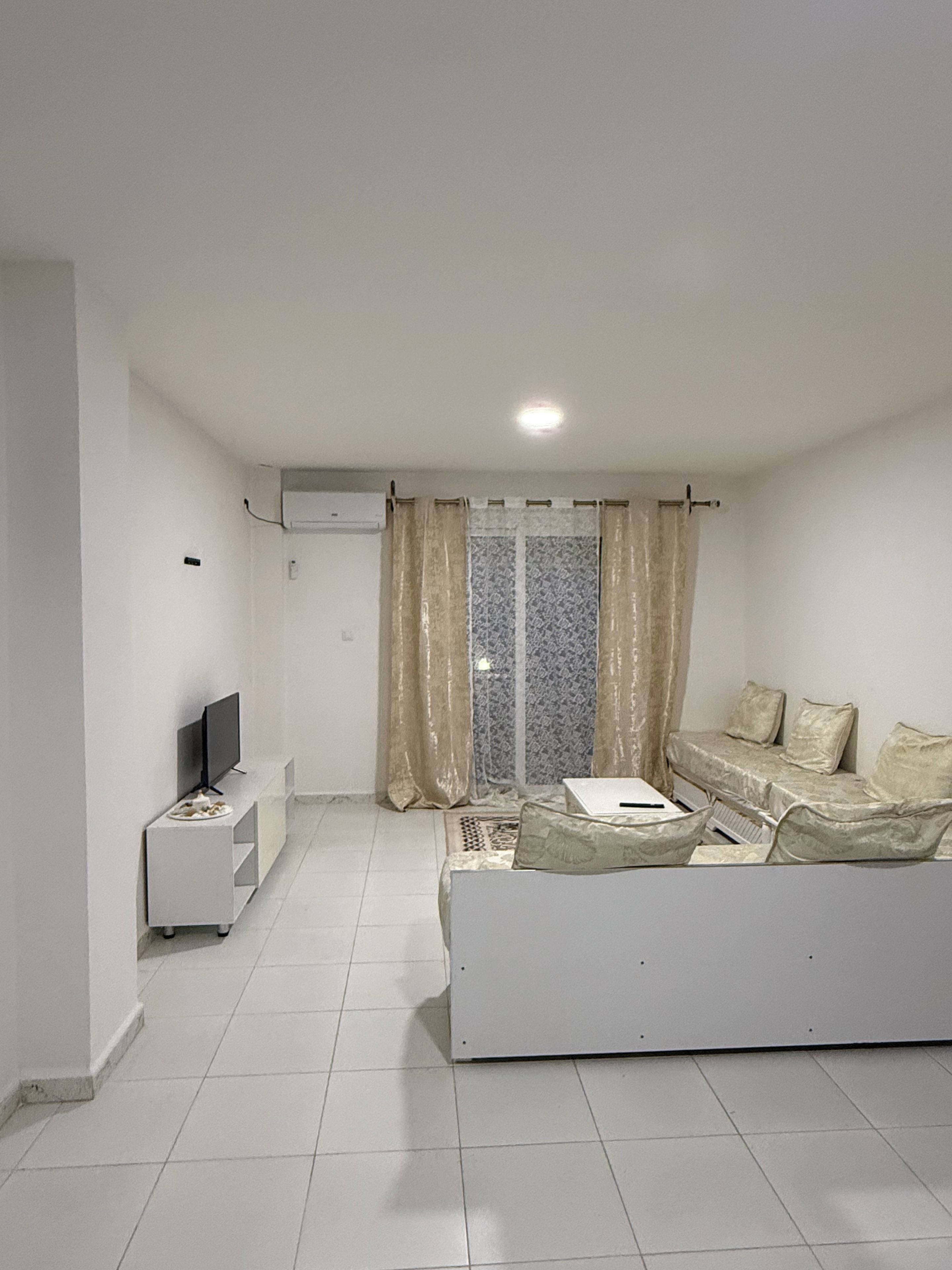 A living room with a sofa, a TV, and a window with curtains.