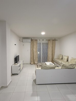A living room with a sofa, a TV, and a window with curtains.
