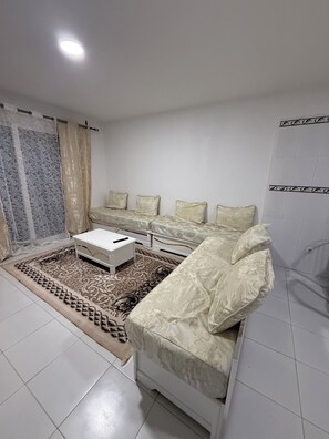 A room with a bed, a white bedside table, and a patterned rug.
