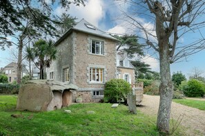 Un bâtiment en pierre avec un toit en pente, un petit jardin avec un arbre et un ciel dégagé.