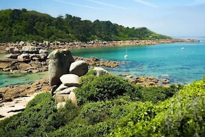 A coastal landscape with rocky formations, clear turquoise waters, and dense greenery.