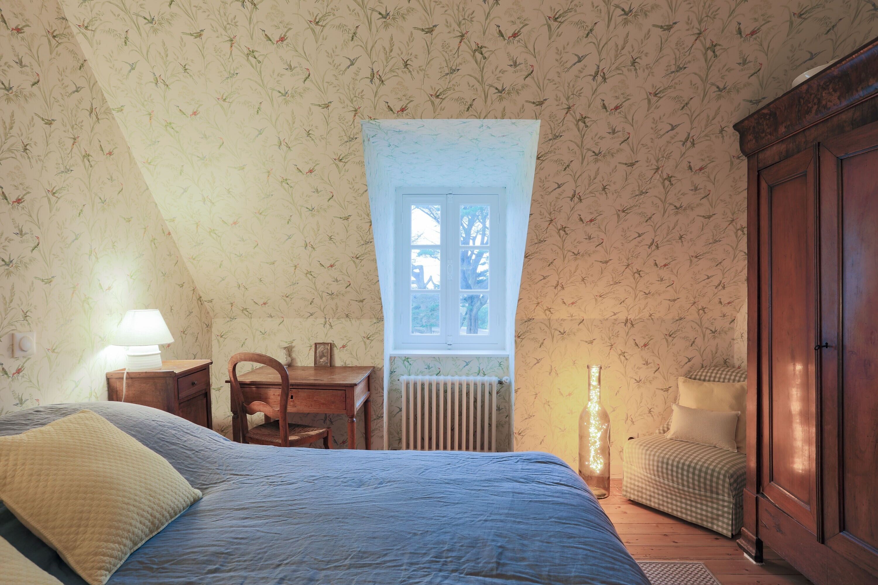 A bedroom with a bed, a desk, a chair, a radiator, and a wardrobe.