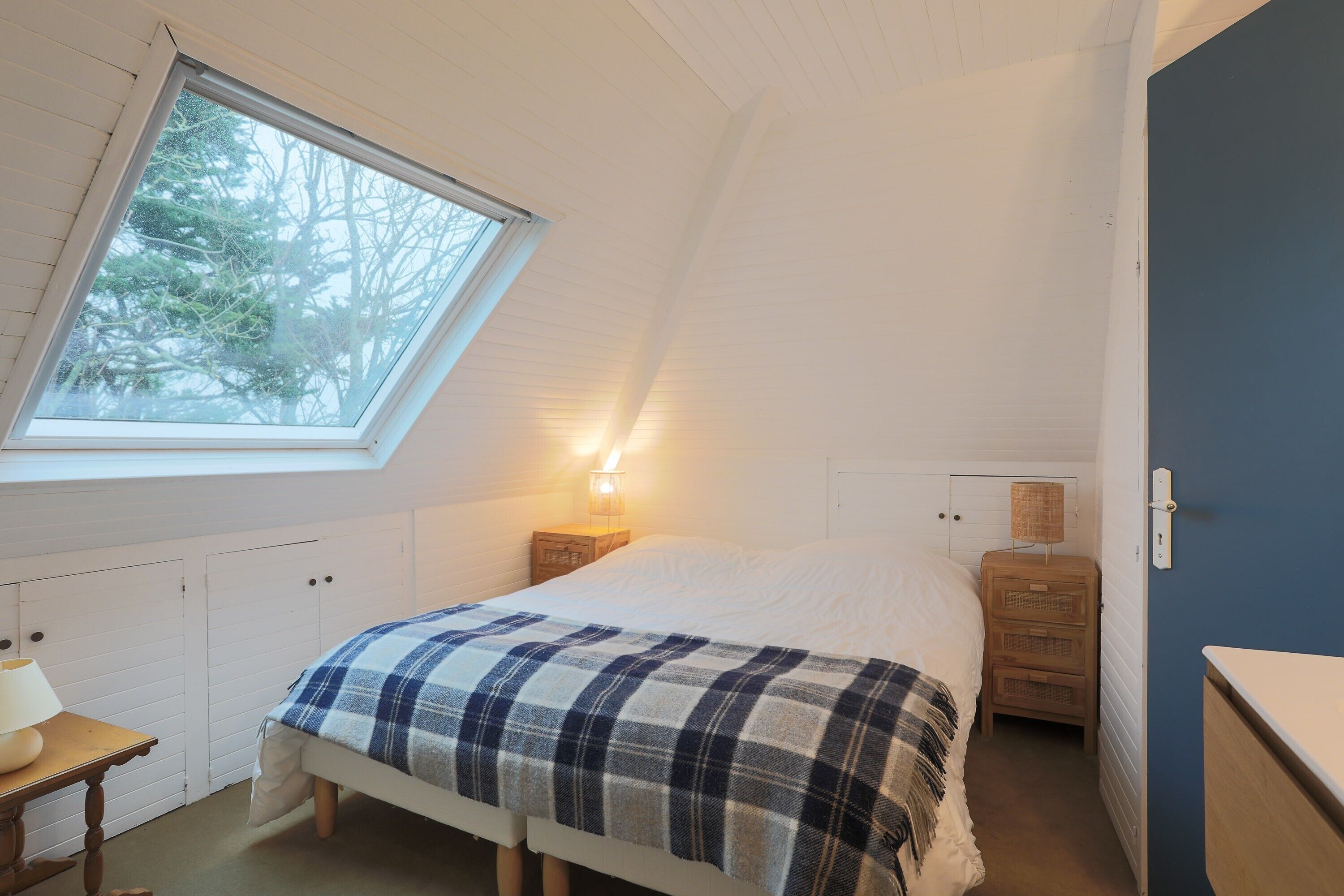 A bedroom with a skylight, a bed with a plaid blanket, bedside tables with lamps, and a dresser.