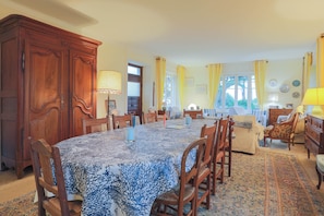 A dining room with a large table, chairs, and a patterned tablecloth.