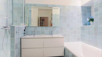 A bathroom with a white vanity, a mirror, a bathtub, and light blue tiles.