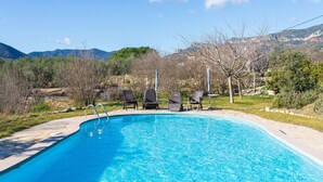 A swimming pool with lounge chairs, surrounded by a landscaped garden and mountains in the background.