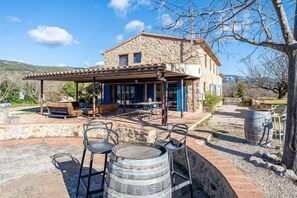 Une maison en pierre avec un patio, des sièges d’extérieur et un tonneau.