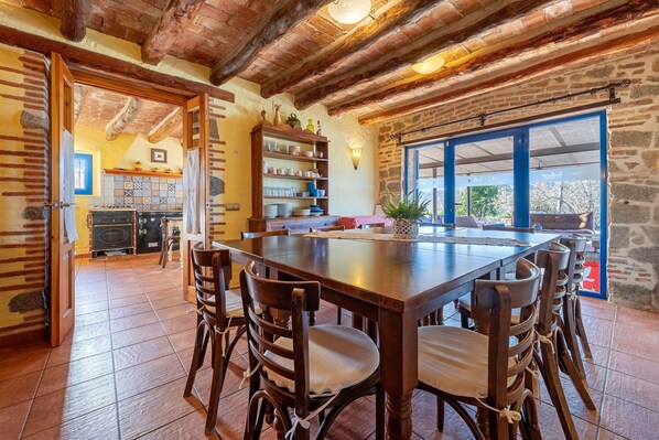 Un coin repas rustique avec une grande table en bois, des chaises et une cuisine en arrière-plan.