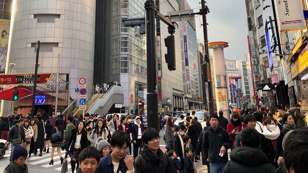 Una calle urbana concurrida con un edificio destacado que presenta un gran anuncio y señalización de Shibuya 109.