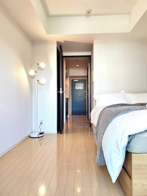 A hotel room with a bed, a bedside table, a lamp, and a door leading to another room.