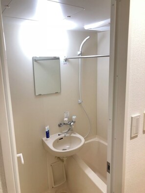 Un baño pequeño y blanco con lavamanos, espejo y ducha.