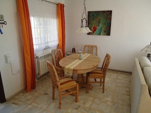 A dining area with a round wooden table, four wooden chairs, a peacock painting on the wall, and a radiator.