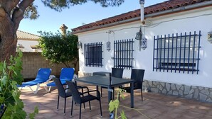 An outdoor patio with a table and chairs, a tree, and a building with barred windows.