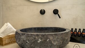 Ein Waschbecken aus Stein, ein Handtuch und ein Flaschenhalter in einem Badezimmer.