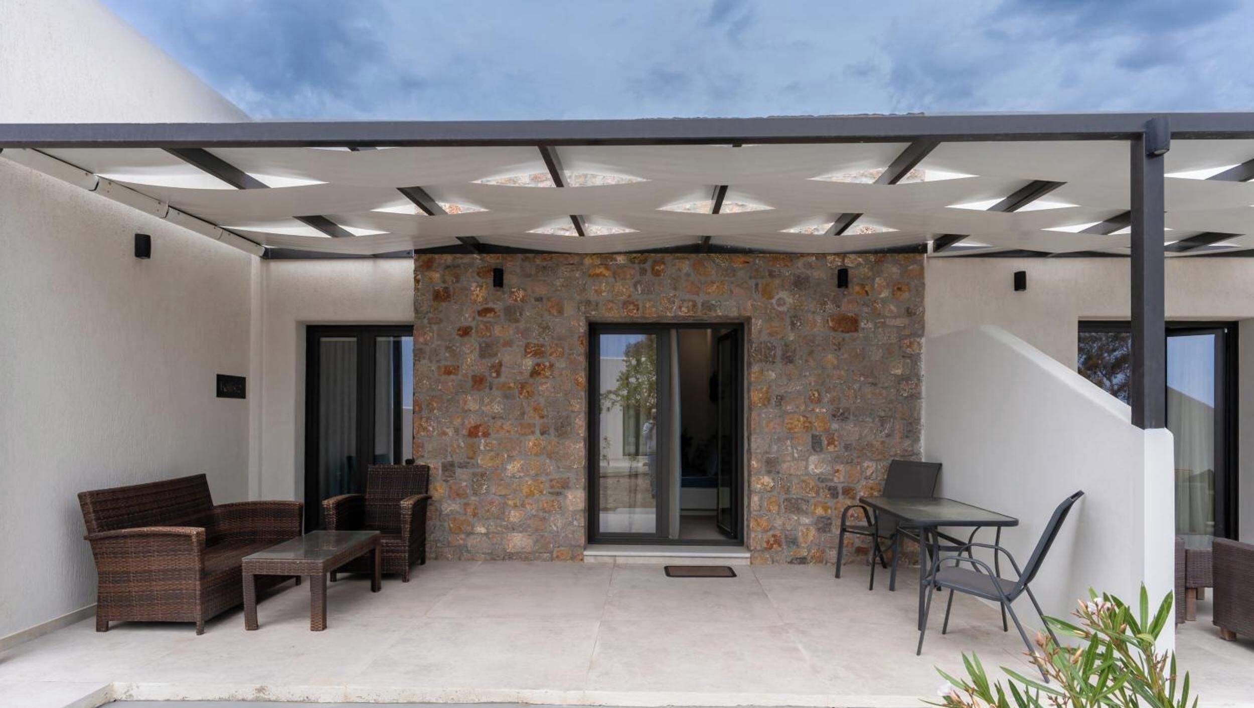 A covered patio with a stone wall, wicker furniture, and a glass table.