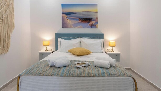 A neatly made bed with towels, a headboard, two bedside lamps, and a painting above.
