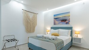 A bedroom with a bed, two bedside lamps, a macrame wall hanging, a small table, and a chair.