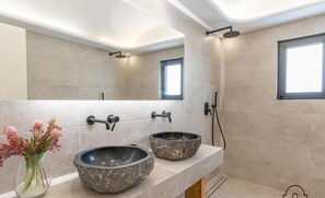Ein modernes Badezimmer mit einem großen Spiegel, zwei Waschbecken aus Stein, einer Dusche und einem kleinen Fenster.