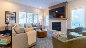 A modern living room with a fireplace, a large TV mounted on the wall, and a cozy seating area with a sofa and armchairs.