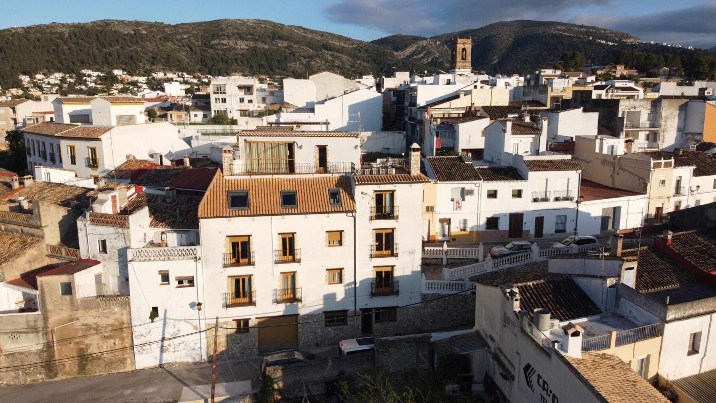 Zona urbana densamente poblada con edificios blancos, algunos con balcones, y una destacada torre de iglesia.