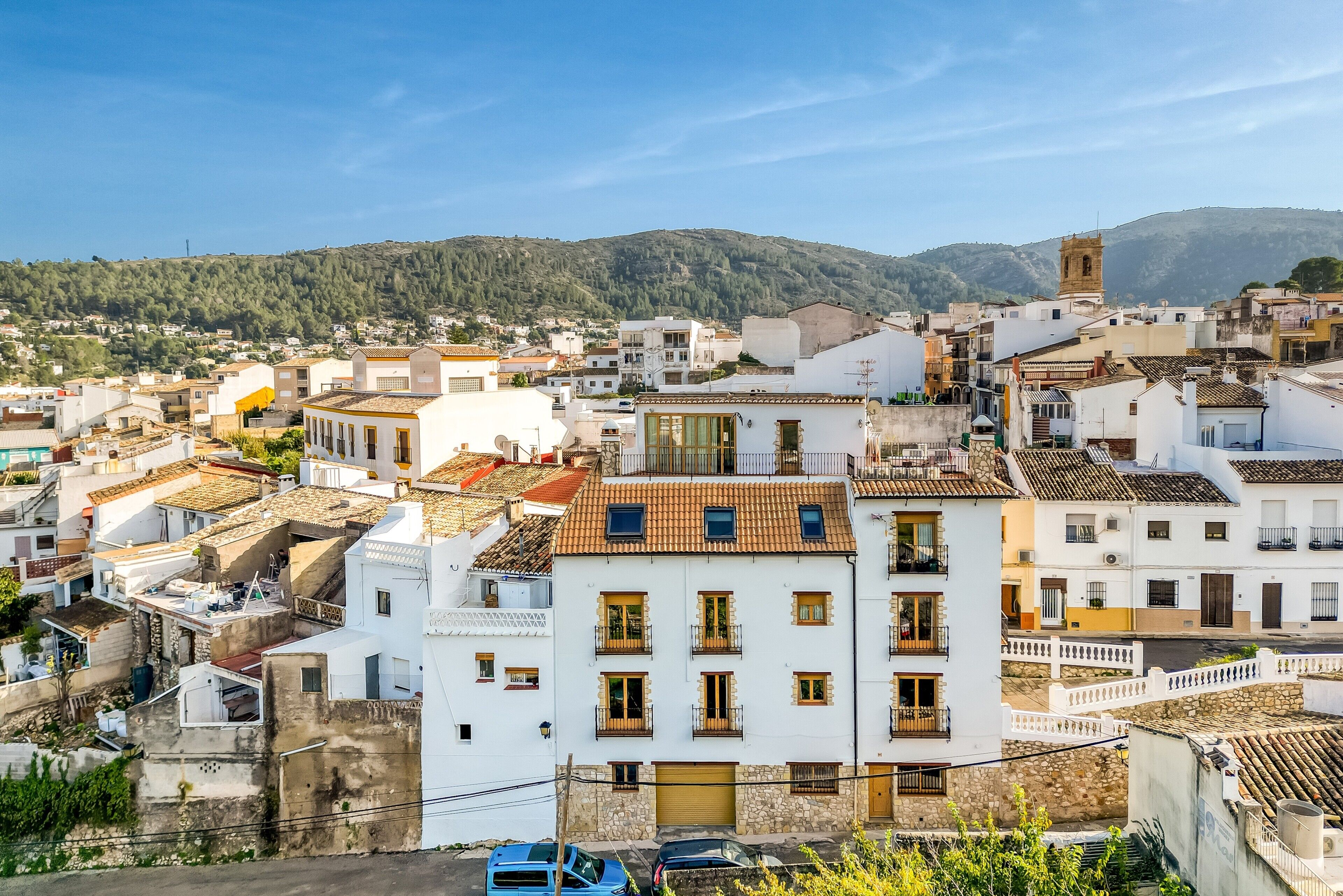 Zona urbana densamente poblada con edificios blancos, una torre destacada y un paisaje montañoso al fondo.