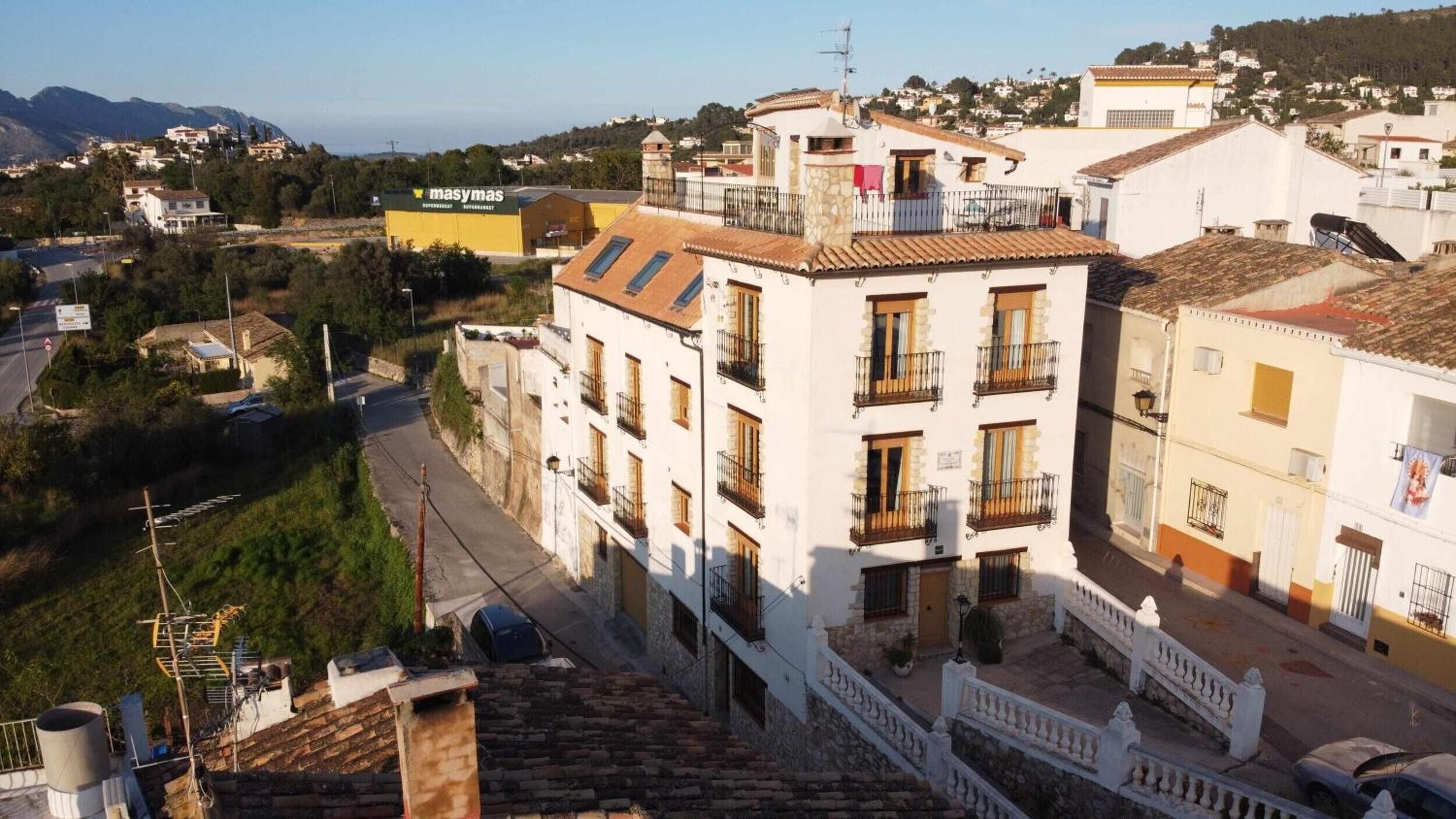 Un immeuble à plusieurs étages doté de balcons, une rue devant et une chaîne de montagnes en arrière-plan.