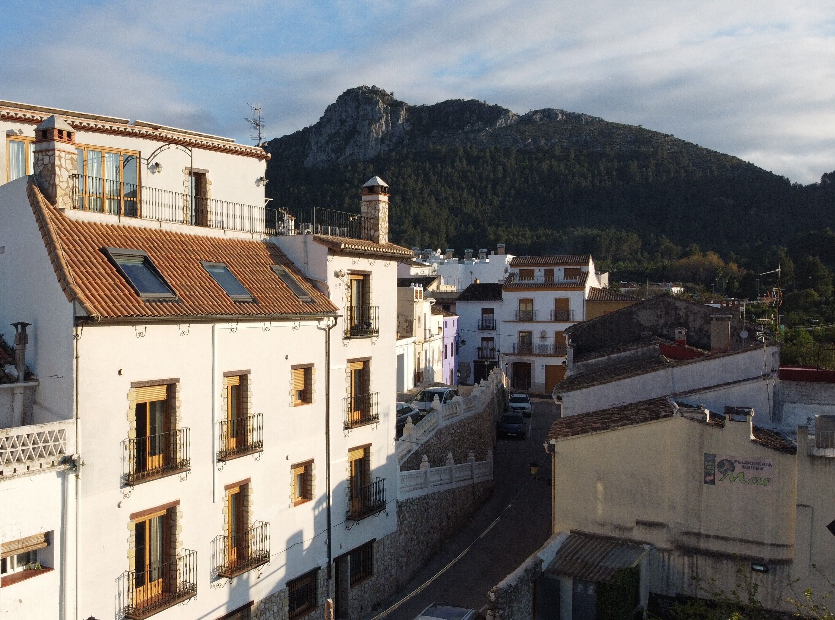 Une rue étroite bordée d’immeubles, une montagne en arrière-plan et une enseigne indiquant « Salon de coiffure mixte ».
