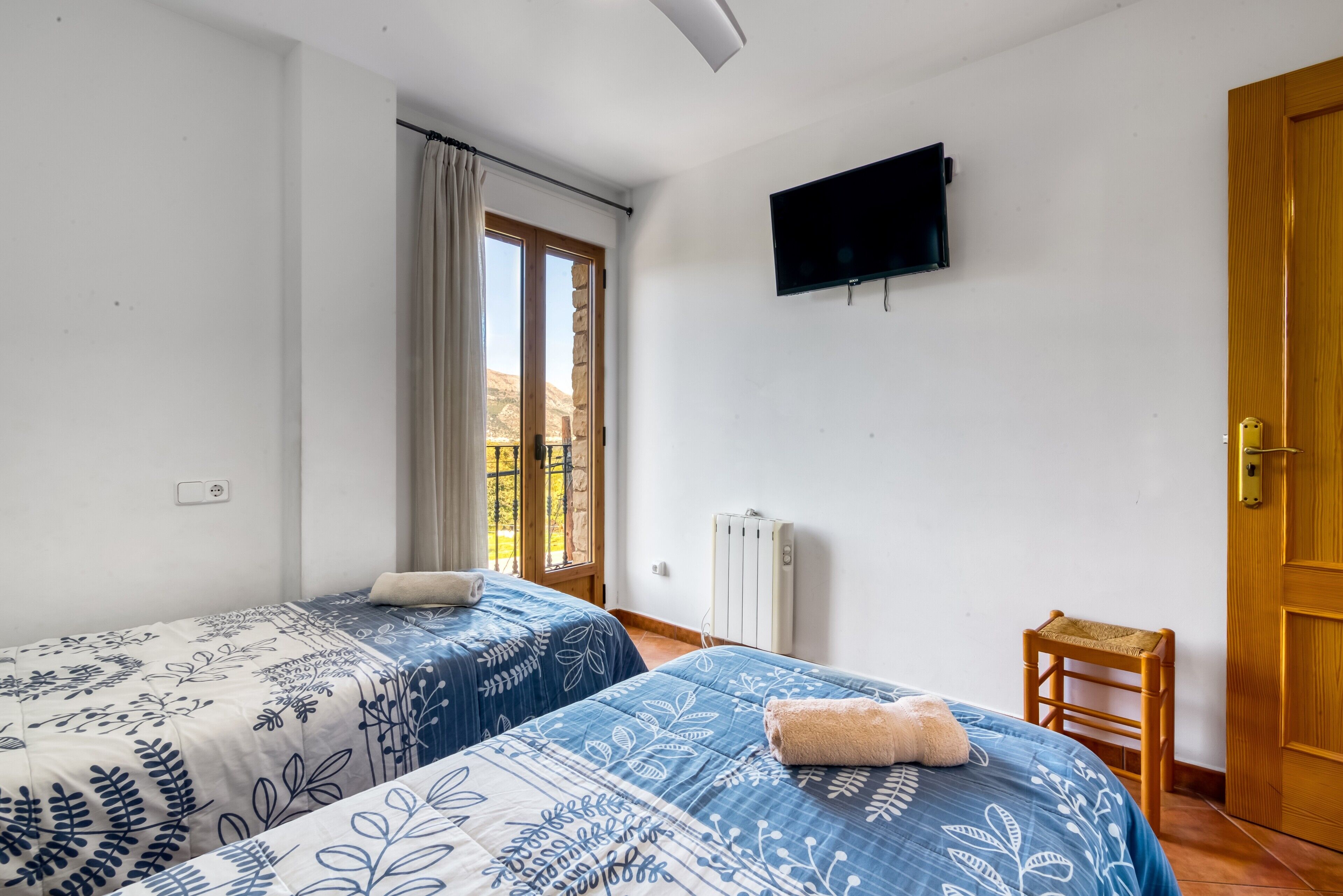 A bedroom with two beds, a TV, a radiator, and a wooden door.
