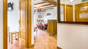 A hallway with wooden doors, a dining area with a table and chairs, and a kitchen area with cabinets and a hanging light fixture.
