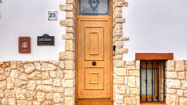 A wooden door with a small window above it, a mailbox, and a number plate on the wall.