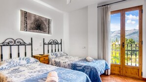 A bedroom with two beds, a nightstand, a painting, and a balcony with a mountain view.
