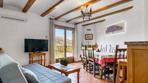 A living room with a sofa, TV, dining table, chairs, and a view of the mountains.