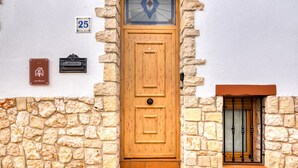 Una puerta de madera con un pequeño ventanal encima, un buzón y una placa de número en la pared.