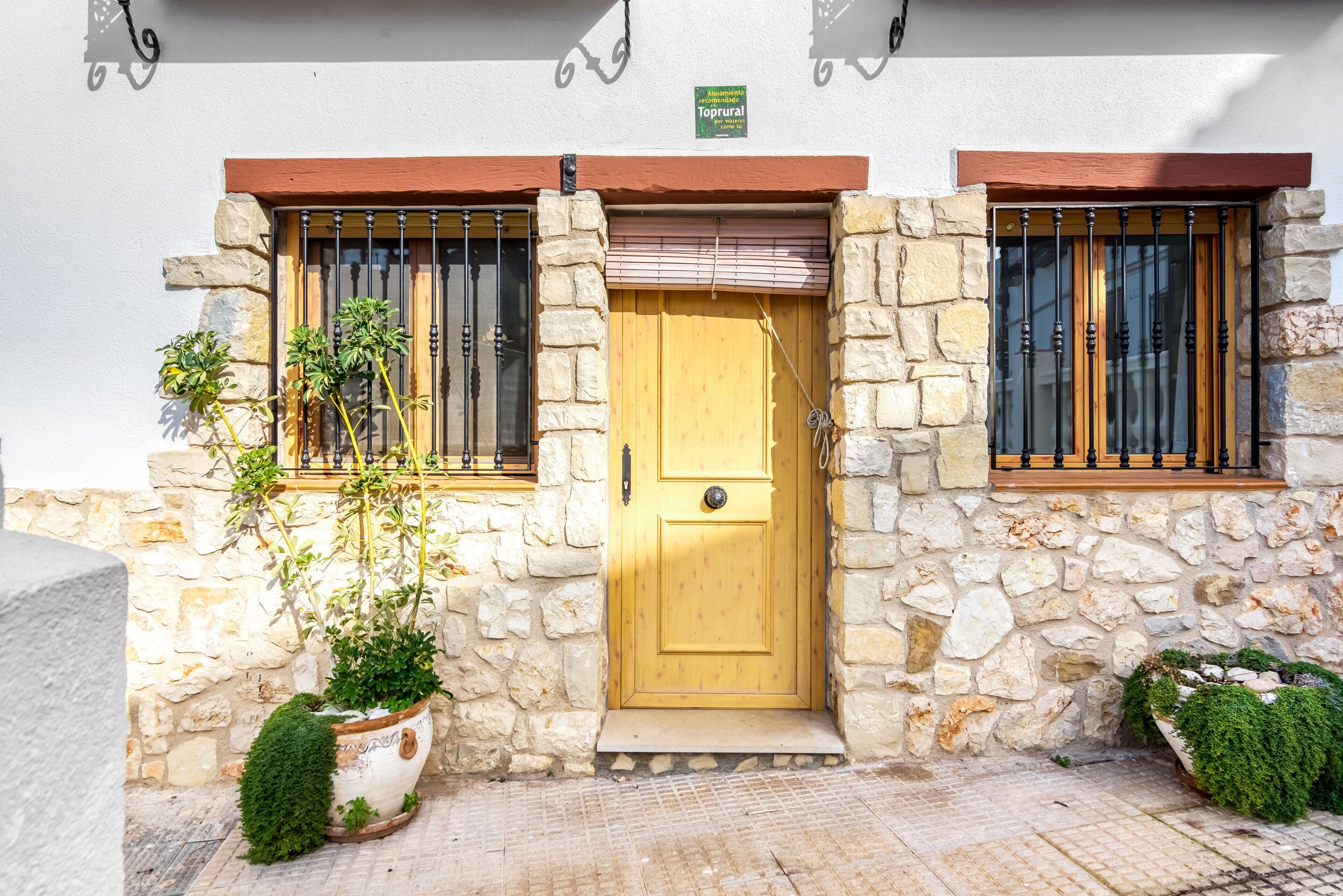 Un bâtiment en pierre avec une porte jaune, deux fenêtres avec des barreaux en métal et une enseigne au-dessus de la porte.