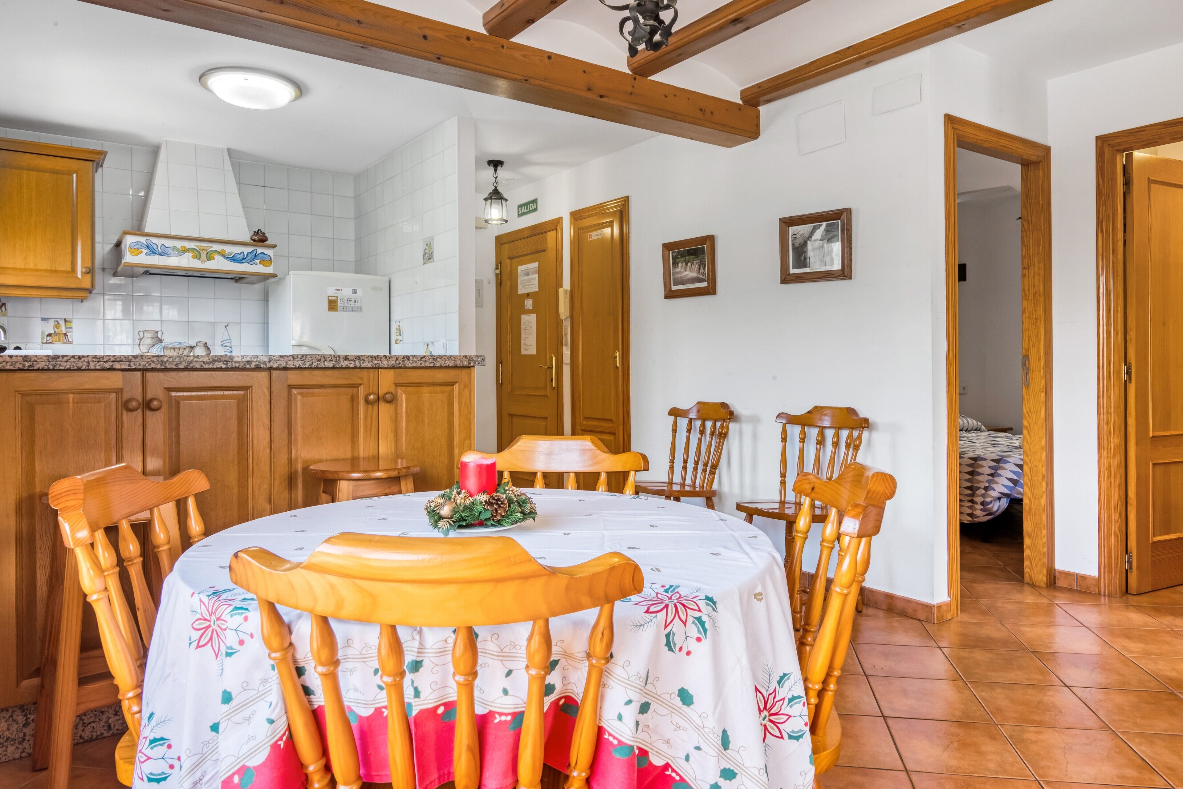 Een eetgedeelte met een ronde tafel, houten stoelen, een witte tafelkleed en een rode kaars als decoratie.