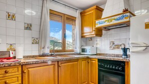 Una cocina con armarios de madera, microondas, lavavajillas y una ventana con vista a las montañas.