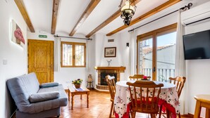 Una sala de estar con sofá, mesa de comedor de madera, sillas, chimenea y televisor montado en la pared.